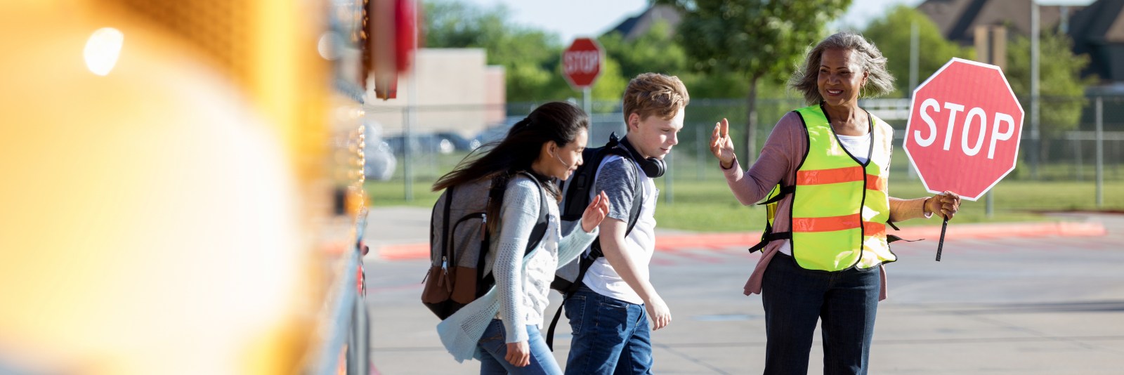 Two kids exit a bus with a crossing guard helping