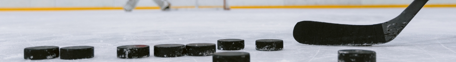 A group of hockey pucks sit on ice with a hockey stick